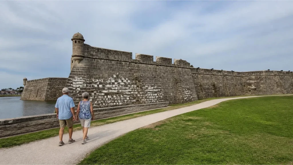 Couple walking along a visitor path beside the stone walls of Castillo de San Marcos in St. Augustine